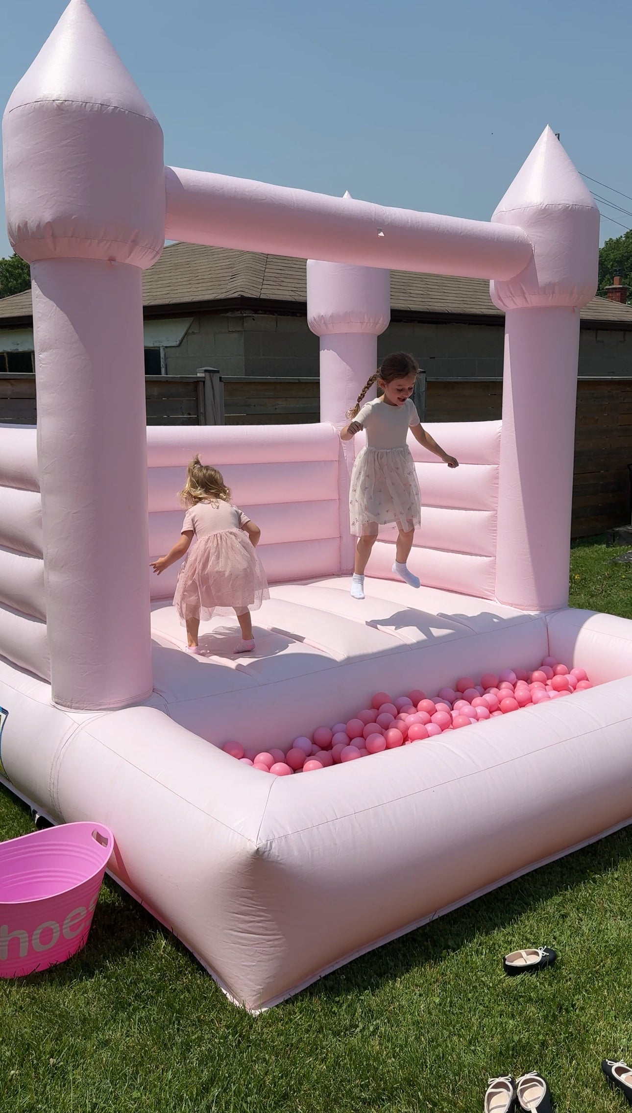 Two children playing in a pink inflatable castle with a ball pit on a grassy area.